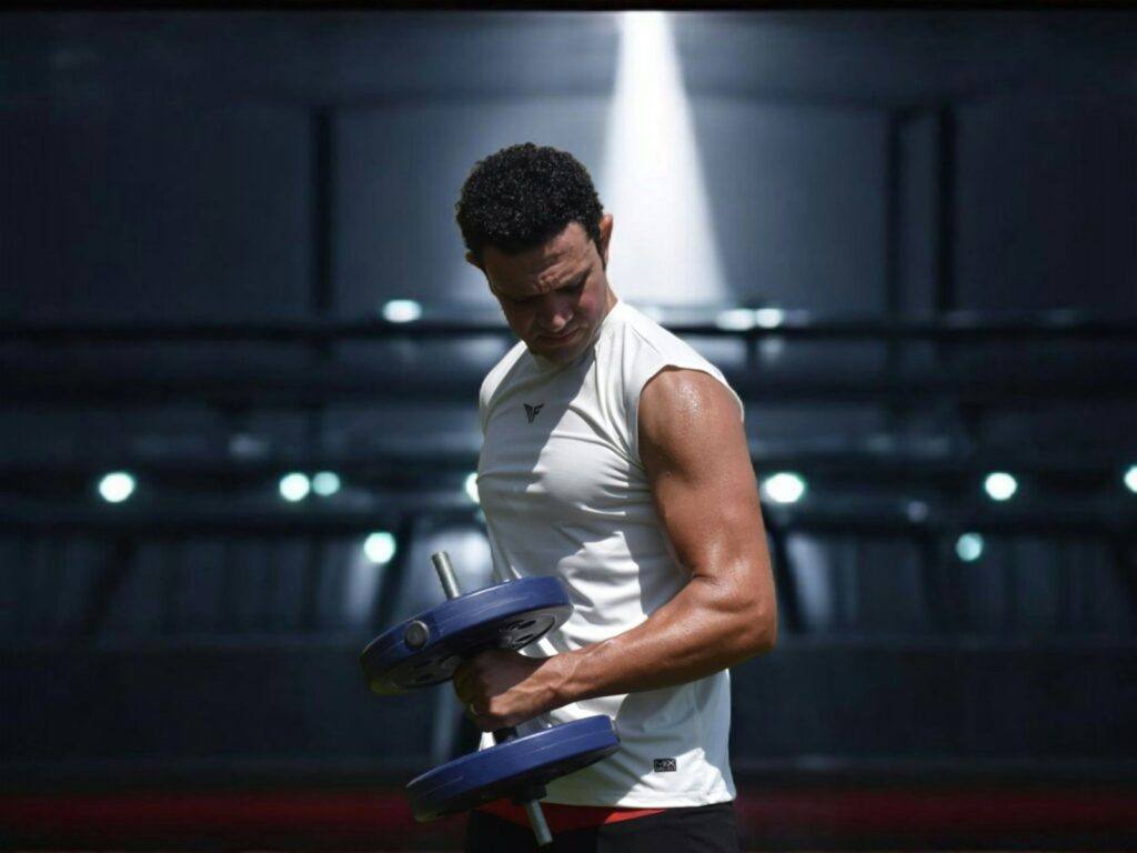 Man lifting dumbbell in a stadium setting with stadium lights